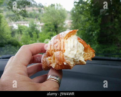 Frau hält köstliche Delikatesse der Brioche mit Vanillesauce. Kuchen zu Essen an der frischen Luft ist sehr gut. Stockfoto