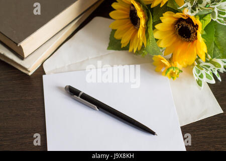 Umschlag mit einem Brief auf einem Holztisch. Bücher, Stift und Blumen. Stockfoto