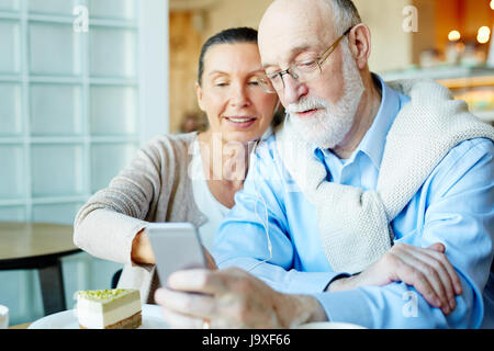 Reifer Mann und Frau mit Kopfhörern, die Auswahl der Tonspur in Smartphone beim Sitzen im café Stockfoto