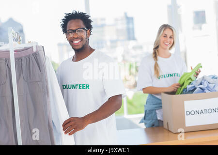 Hübsche Freiwilligen unter Kleidung aus einer Spendenbox in ihrem Büro Stockfoto