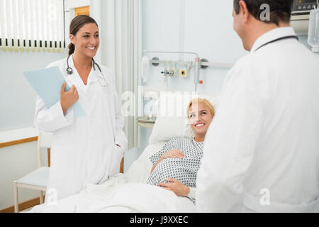 Weibliche und männliche Ärzte stehen neben einem Patienten in einem Krankenhausbett Stockfoto