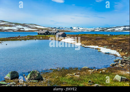 Isolierte Häuser mit blauen See und eine schöne Landschaft von Hügeln teilweise mit weißen Schnee in Norwegen umgeben Stockfoto