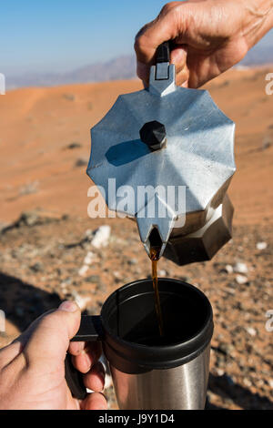 Frau gießen Kaffee auf einem camping Cup mit der Wüste im Hintergrund Stockfoto