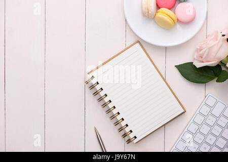 Weißer Schreibtisch mit bunten Macarons, Tastatur und offene Notebook. Stockfoto