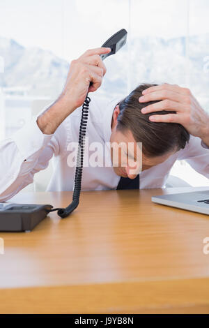 Gereizte Geschäftsmann hält das Telefon in seinem Büro Stockfoto