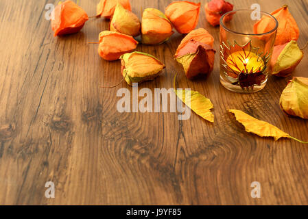 chinesische Lapion Pflanze Früchte auf Tisch mit brennenden Teelicht im Glas. herbstliche Dekoration mit Textfreiraum Stockfoto