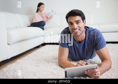 Mann mit einem Tablet-Computer während seiner Verlobten ein Buch in ihrem Wohnzimmer liest Stockfoto