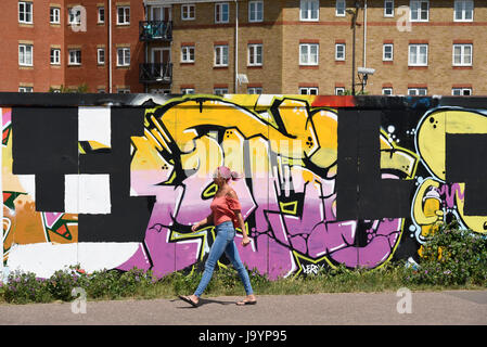 Eine Frau, die an Graffiti auf einer Baustelle vorbeiläuft und hortet. Graffiti über Arbeit von John Bulley in Southend on Sea, Essex Stockfoto