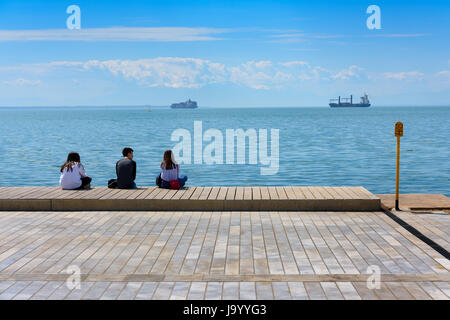 Junge Menschen genießen Sommernachmittag an der Pier von Thessaloniki, Griechenland mit mehreren Schiffen im Hintergrund Stockfoto