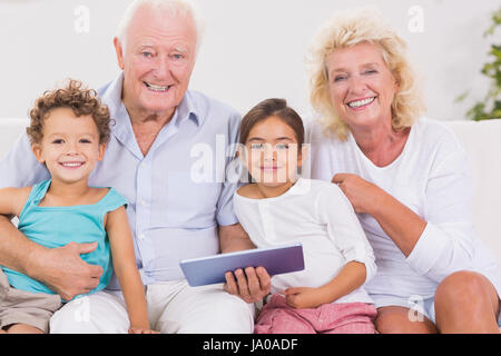 Lächelnd Großeltern mit Kindern bei der Nutzung eines Tablet PCs auf dem sofa Stockfoto