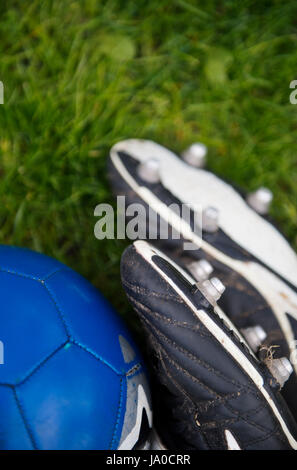 Paar schwarze Fußballschuhe und einen blauen Fußball auf einer Wiese Stockfoto