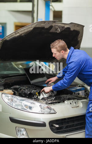 Kfz-Mechaniker mit Laptop Reparatur Automotor in Werkstatt Stockfoto