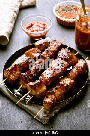 Gegrillte Schweinefleisch-Spieße auf Platte über dunklem Stein Stockfoto