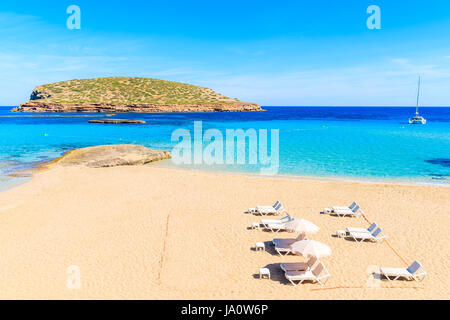 Blick auf Cala Comte-Strand mit Liegestühlen und Sonnenschirmen - berühmt für seine Azure kristallklares seichten Meerwasser, Insel Ibiza, Spanien Stockfoto