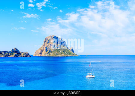 Blick auf Es Vedra Insel und Katamaran Boot am blauen Meer in Cala d ' Hort Bucht, Insel Ibiza, Spanien Stockfoto