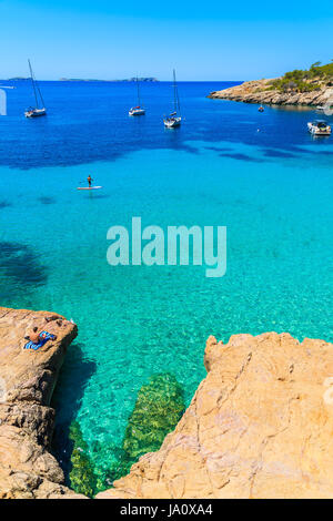 Unbekannter Mann touristischen Sonnenbaden auf einem Felsen in der Bucht Cala Salada mit Meerblick Bucht, Insel Ibiza, Spanien Stockfoto