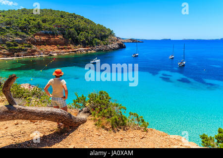 Junge Frau Tourist auf Fels-Klippe stehend und mit Blick auf die Bucht Cala Salada berühmt für seine Azure kristallklares Meerwasser, Ibiza Insel, S Stockfoto