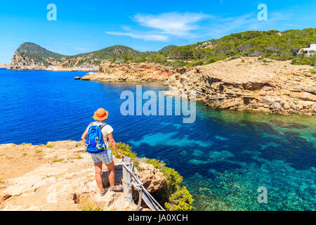 Junge Frau touristischen Backpacker stehen auf Felsen und mit Blick auf Punta Galera Bucht umgeben von erstaunliche Steinformationen, Insel Ibiza, Spanien Stockfoto