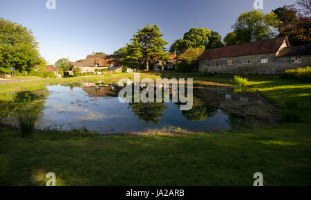 Traditionellen strohgedeckte Hütten spiegeln sich in der Tau-Teich in der englischen Dorf Ashmore, Dorset. Stockfoto