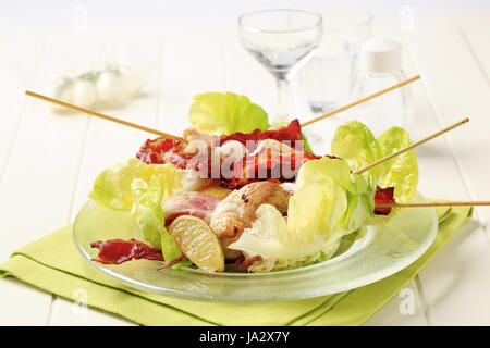 Gebratene Hähnchen-Spieße und Speck serviert auf Salatblättern Stockfoto