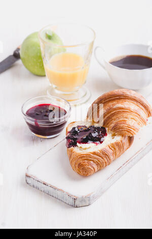 Frühstück auf weißem Holz - Croissant, Marmelade, Orangensaft und Kaffee Stockfoto