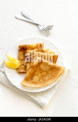 Crepes Suzette mit Zitrone auf weißen Teller über weißem Hintergrund kopieren Raum. Köstliche hausgemachte Pfannkuchen zum Frühstück. Stockfoto