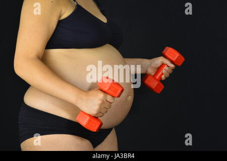 Eine schwangere Frau in Form von kleinen roten Gewichte heben zu bleiben. Stockfoto