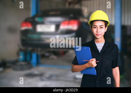 Porträt von lächelnden jungen weiblichen Mechaniker Inspektion auf einen Mietwagen in Autowerkstatt Stockfoto