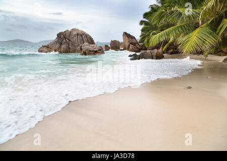 Schöner Strand Anse Patates, La Digue, Seychellen mit Granitfelsen und Palmen an einem bewölkten Tag Stockfoto