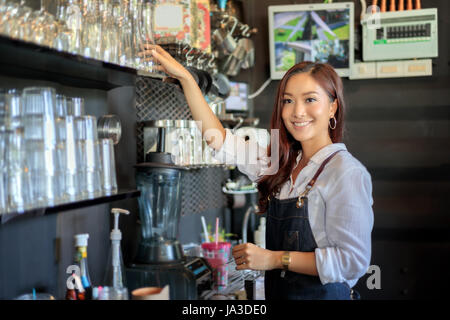 Asiatische Frauen Barista lächelnd und mit Kaffee aus dem Automaten im Kaffee shop counter - arbeitenden Frau Kleinunternehmen Besitzer Essen und trinken Café-Konzept Stockfoto