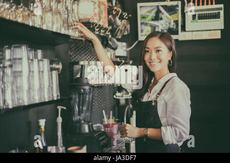 Asiatische Frauen Barista lächelnd und mit Kaffee aus dem Automaten im Kaffee shop counter - arbeitenden Frau Kleinunternehmen Besitzer Essen und trinken Café-Konzept Stockfoto
