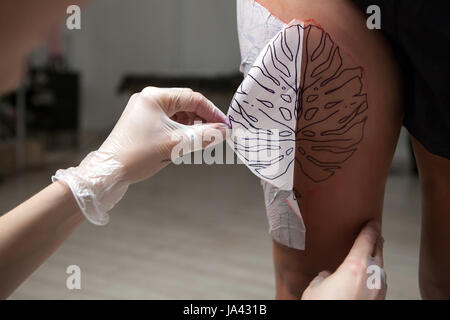 Ein professioneller Tätowierer wird mit Skizze auf das Körperteil vorgestellt. Stockfoto