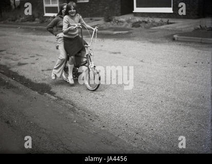 1970er-Jahren, historische, zwei junge Mädchen, die mit dem toskanischen Fahrrad, ein Chopper Art Fahrrad mit hoher Lenker und verschiedene große Räder, eine kultige Motorrad dieser Epoche. Stockfoto