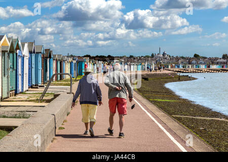 EIN ÄLTERES EHEPAAR ZU FUß ENTLANG DER STRANDPROMENADE BRIGHTLINGSEA IN ESSEX. DER MANN SCHEINT ZU EINEN KAPUTTEN RÜCKEN LEIDEN. Stockfoto