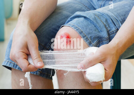 Man heilt die Wunde am Knie zu Hause. Die Bandage halten an den Händen Stockfoto