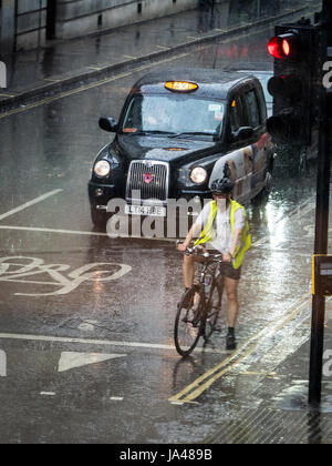 Londoner Radfahrer und Londoner Taxi Black Cab warten bei starkem Regen in der Londoner Innenstadt, Großbritannien, an der Ampel Stockfoto