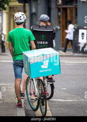 Deliveroo und Uber frisst Lebensmittel Lieferung Fahrradkuriere warten an der Ampel bei der Bereitstellung von Nahrung für Kunden im Zentrum von London. Stockfoto