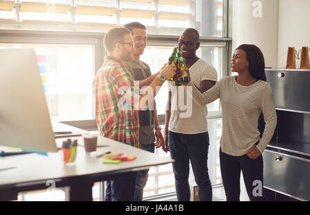 Lächelnde junge Gruppe von Büroangestellten ruht mit dem Bier im Büro. Stockfoto