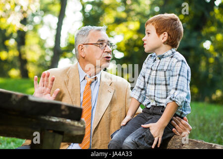 Großvater und Enkel sitzen und reden im park Stockfoto