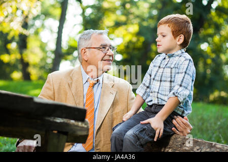 Großvater und Enkel sitzen und reden im park Stockfoto