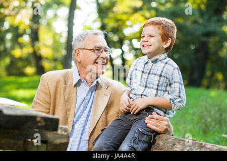 Großvater und Enkel sitzen und reden im park Stockfoto