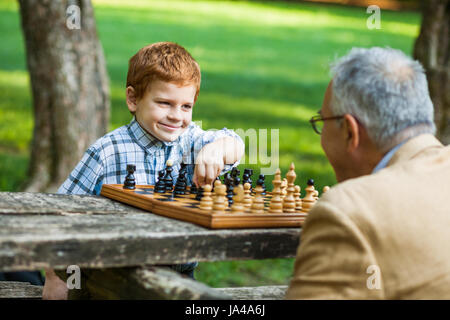 Großvater und Enkel spielen Schach im park Stockfoto