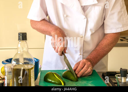 Ältere Mann in der Köche weiß schneiden Avocado auf Schneidebrett in der Küche, Schottland, Großbritannien Stockfoto