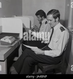 der 1970er Jahre hat zwei uniformierte Polizisten sitzen an den Ständen mit dem neuen Diktiergerät oder Audio-Aufnahme Maschinen der Metropolitan Police Service Datei Erklärungen oder Berichte eingeführt. Stockfoto