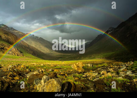 Eine doppelte leuchtenden Regenbogen nach dem Regen zu den hohen Bergen des Tals: über den grünen Feldern ist ein schöne, helle Regenbogen Bogen, ein Sommertag, der Himalaya. Stockfoto