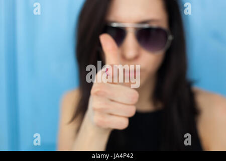 Verschwommenes Portrait eines Mädchens in Sonnenbrillen. Sie verweist auf den Zeigefinger auf den Betrachter. Stockfoto