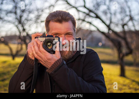 Ein reifer Mann nimmt Bilder auf eine spiegellose Kamera auf der Straße. Hobby der Fotografie. Neue Trends in der Fototechnik. Stockfoto