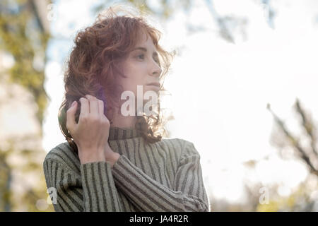 Ein rothaariges Mädchen mit locken im Park steht und schaut leider Weg. Stockfoto