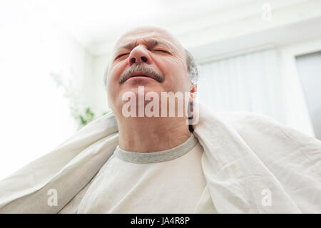 Ein älterer Mann leidet unter Schmerzen und Stress. Er warf eine weiße Decke über die Schultern. Stockfoto