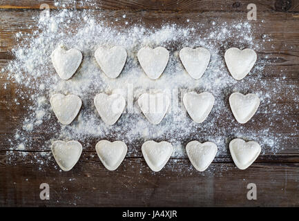 Herzförmige Ravioli mit Mehl auf Vintage Holztisch Hintergrund. Knödel kochen. Ansicht von oben. Stockfoto